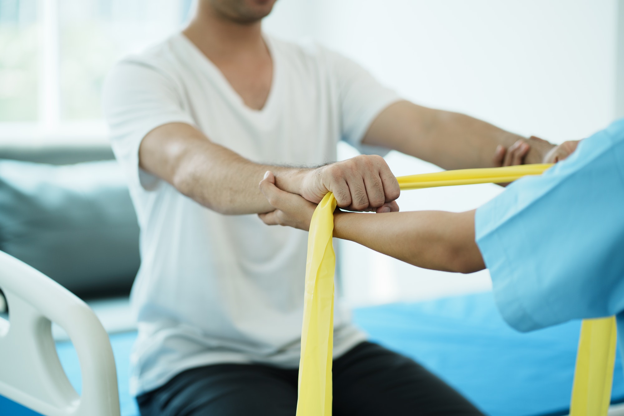Close up hand patient doing stretching exercise with a flexible exercise band and a physical therapi